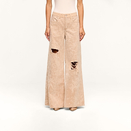 Wearing the Quincy Embellished Wide-Leg Jean in beige—high-rise, wide-leg pants featuring a distinctive crushed velvet texture and distressed rips on the right thigh and knee—paired with beige pointed-toe shoes. The upper body is not fully visible.