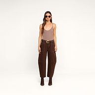 A woman wearing sunglasses, a beige tank top, the Cody Cropped Barrel-Leg Jean in brown with large pockets, a wide belt, and brown boots stands against a plain white background.