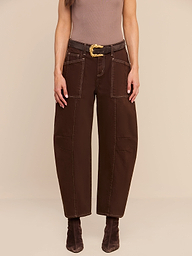Person wearing the Cody Cropped Barrel-Leg Jean, styled with a brown belt, pointed brown boots, and a sleeveless brown top, standing against a plain white background. Only the lower half of the body is visible.