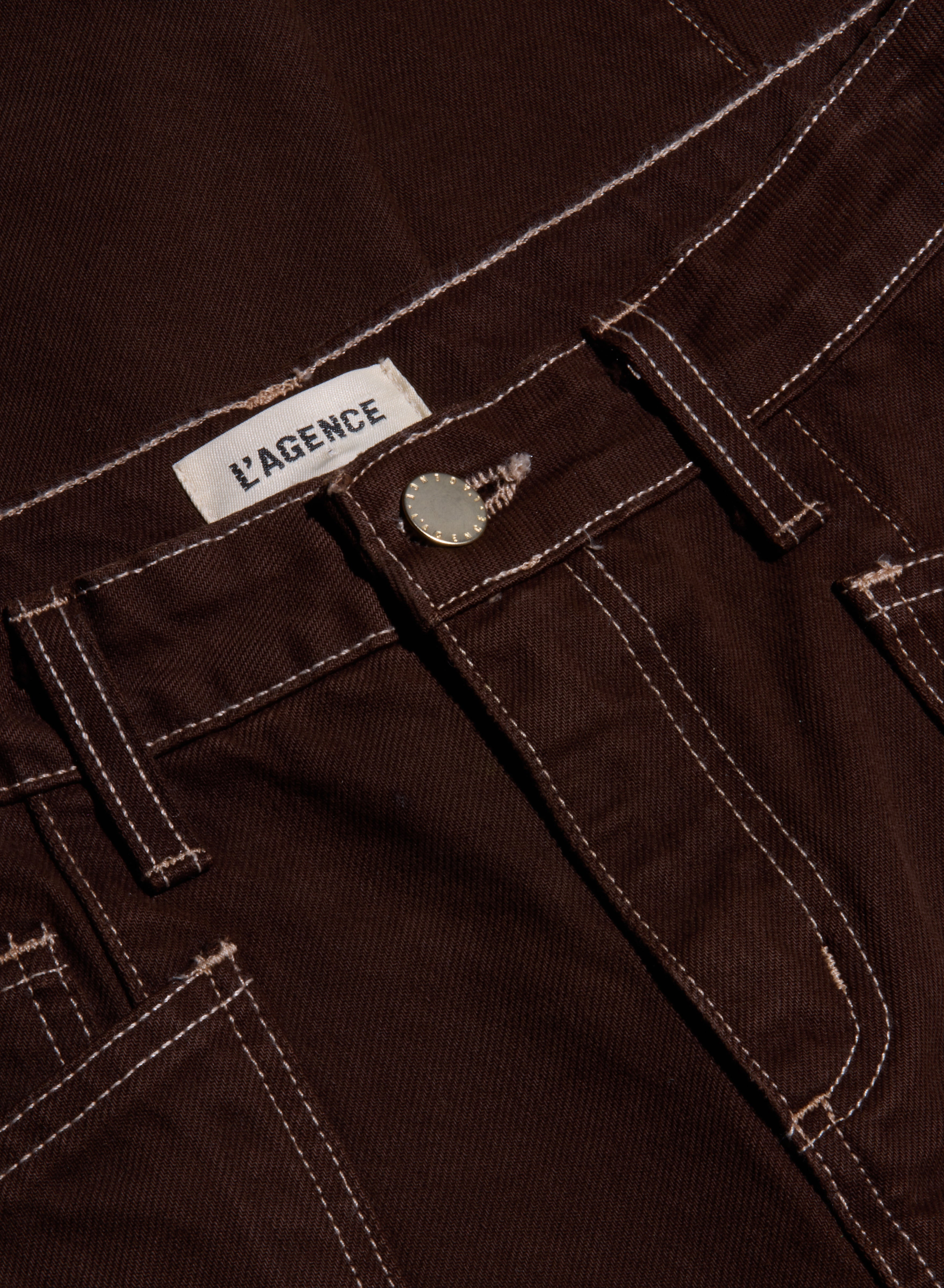 Close-up of the Cody Cropped Barrel-Leg Jean in brown high-rise denim, featuring white stitching, a metal button, and a visible L’AGENCE brand label on the waistband. Crafted from non-stretch denim with a modern barrel-leg silhouette.
