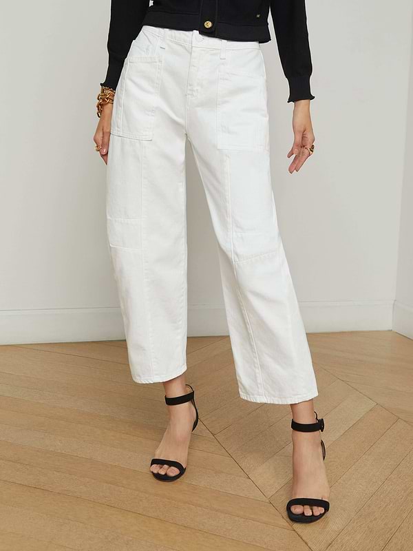 A person wearing the Cody Barrel-Leg Jean in a high-rise white denim style, paired with black heeled sandals, a black long-sleeve top, and bracelets, stands against a plain light background.