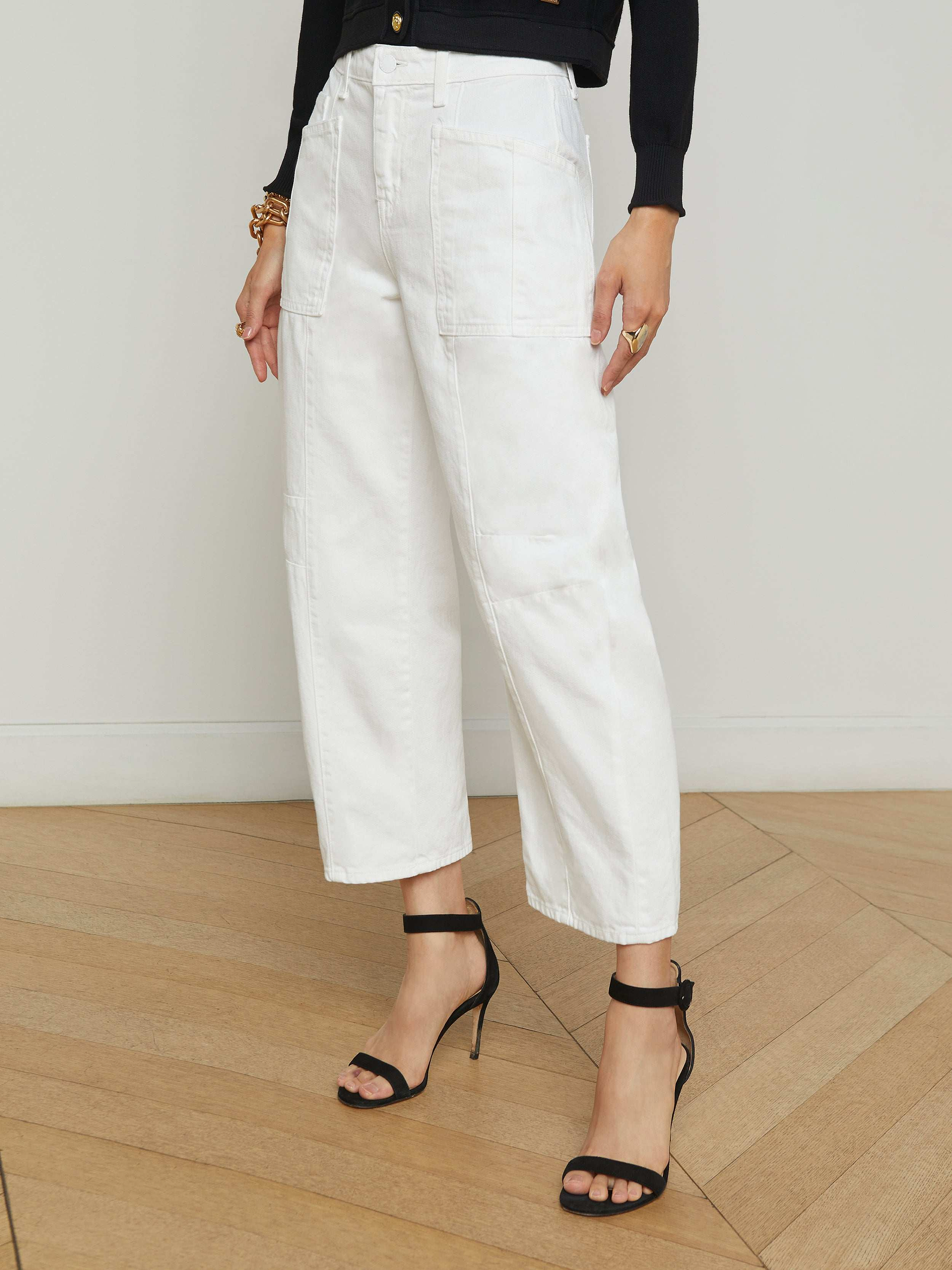 Wearing the Cody Barrel-Leg Jean in a high-rise white denim, paired with black high-heeled sandals, a person stands against a light background; the upper body is mostly out of frame.