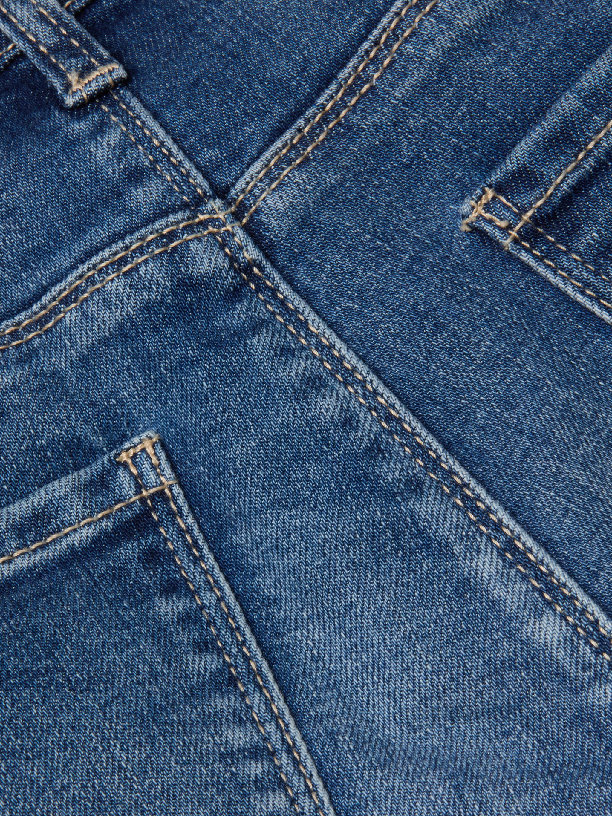 Close-up of the Cara Low-Rise Bootcut Jean in stretch denim blue, highlighting the back pockets, seams, and distinctive orange stitching. The texture and weave of the fabric are clearly visible.