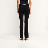 A person stands facing away, wearing the Cara Low-Rise Bootcut Jean in black stretch denim, paired with a black belt, a sleeveless black top, and black heeled shoes against a plain white background.