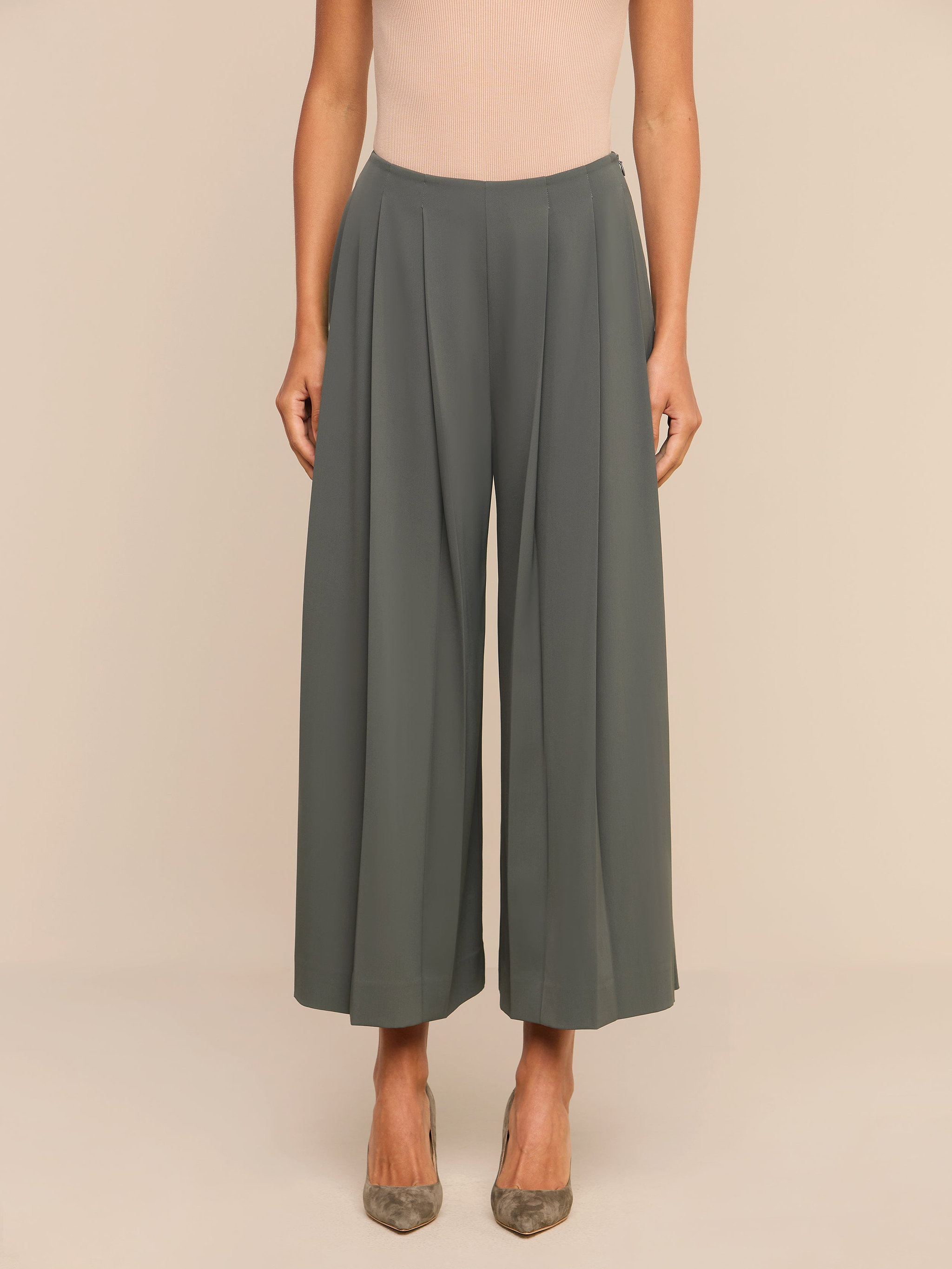 A person wearing Novalynn Cropped Pleated Pant in olive green and beige pointed-toe heels stands against a plain white background.
