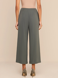 A woman stands facing away, wearing high-rise olive green Novalynn Cropped Pleated Pants with wide legs, a beige sleeveless top, and taupe high heels against a plain white background.