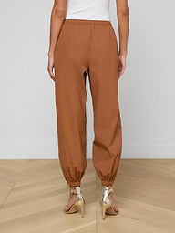 A person is shown from the back against a plain light background wearing the Mariko Jogger—modern brown jogger pants crafted from water-repellent nylon—and beige high-heeled sandals.