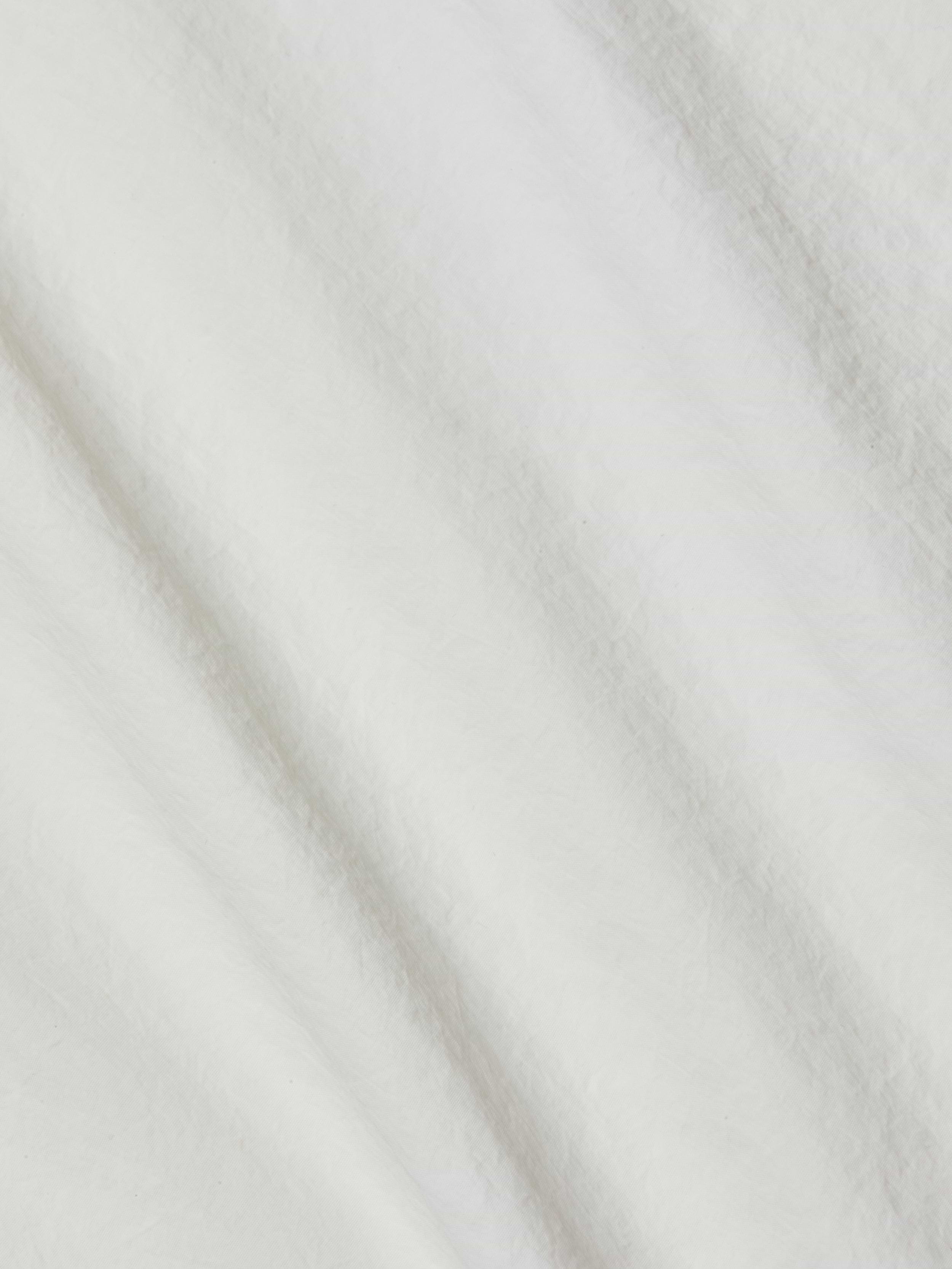 A close-up of the soft, ivory fabric of the Mariko Jogger reveals delicate texture with subtle diagonal folds and shadows. The material looks fluffy and smooth—reminiscent of fleece or cotton, yet crafted from water-repellent nylon for a modern finish.