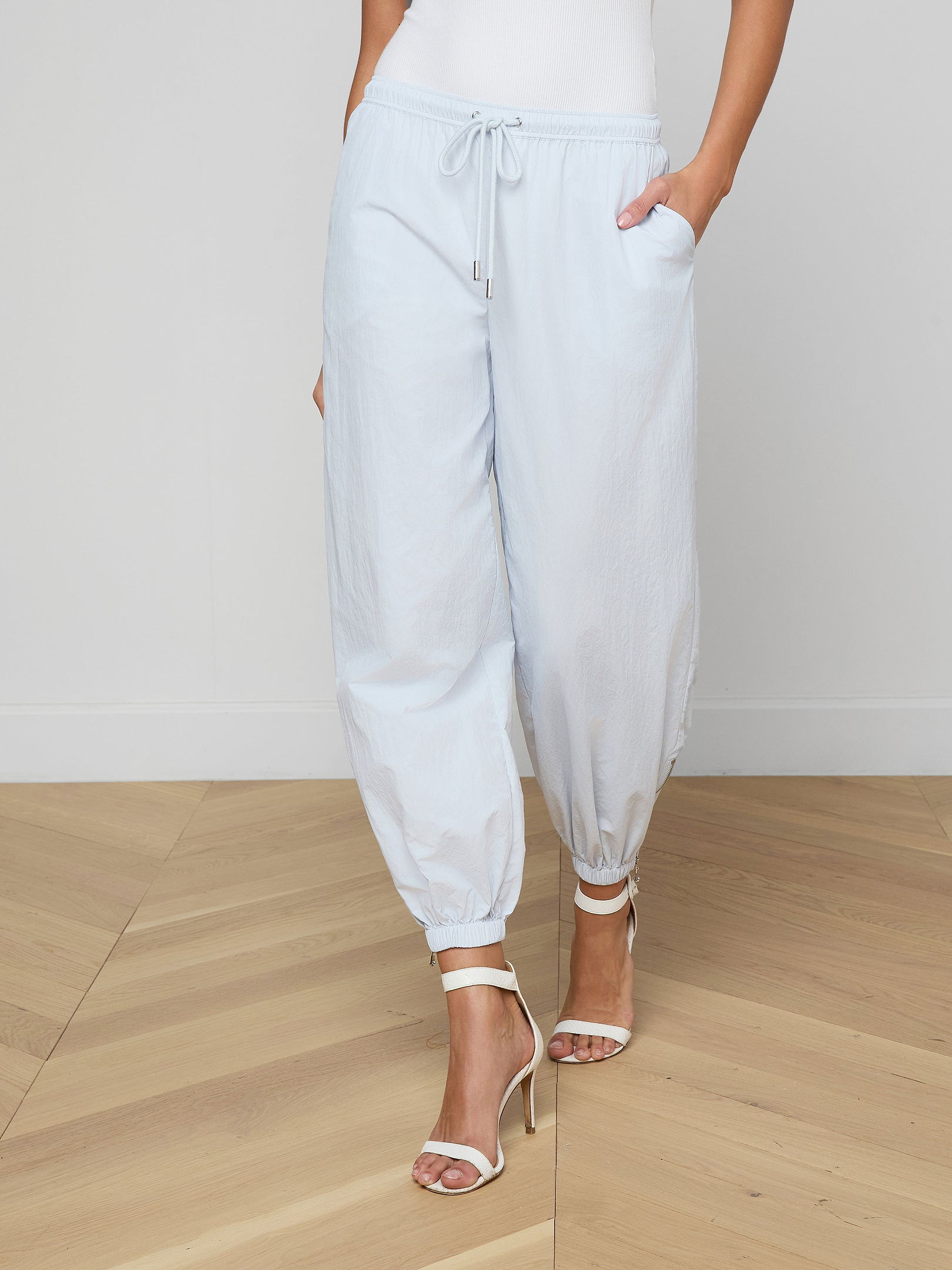 A person wearing the Mariko Jogger in light blue paired with white high-heeled sandals, standing with hands in pockets against a plain light background.