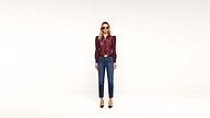A woman wearing sunglasses, a burgundy long-sleeve top, blue jeans, and burgundy heels stands against a plain white background.