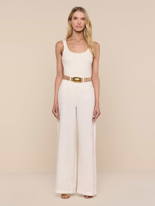 A woman stands facing forward against a plain white background, wearing a beige tank top, the Amara Linen Wide-Leg Pant, a tan belt with a gold buckle, and sandals.