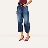 A woman wearing Mallis Bow-Leg Jeans in indigo wash, styled with a brown belt, a burgundy top, and matching burgundy high-heeled shoes, stands against a plain light background.