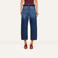 A person is shown from the back wearing the Mallis Bow-Leg Jean in an indigo wash paired with red high-heeled shoes. Their arms are relaxed at their sides, and the background is plain and light-colored.