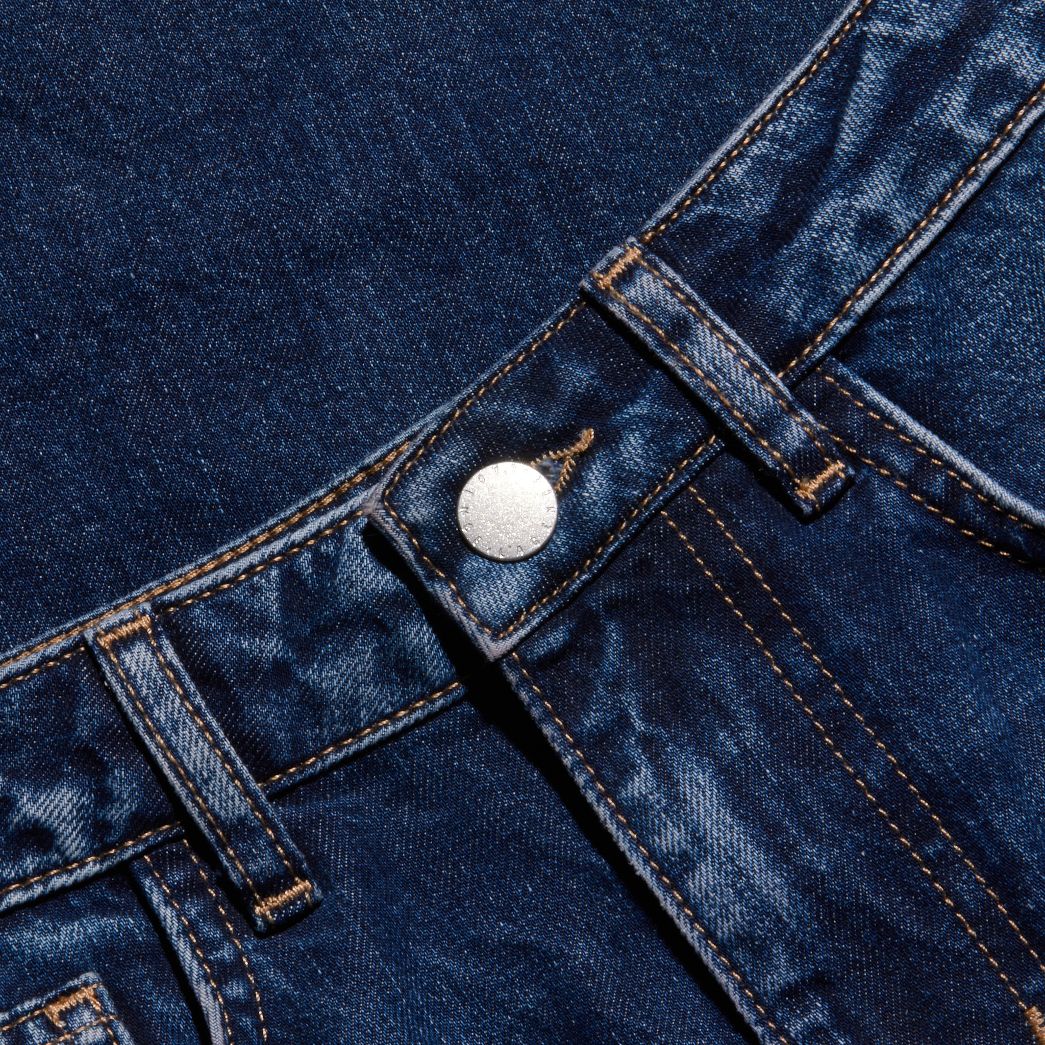 Close-up of dark blue denim jeans showcasing the waistband, belt loops, metal button, and distinctive orange stitching details.