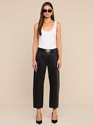 A woman stands against a plain white background, facing forward with her arms relaxed by her sides, wearing sunglasses, a white tank top, black heels, and the Mallis Coated Bow-Leg Jean in a high-rise, wide-leg silhouette.