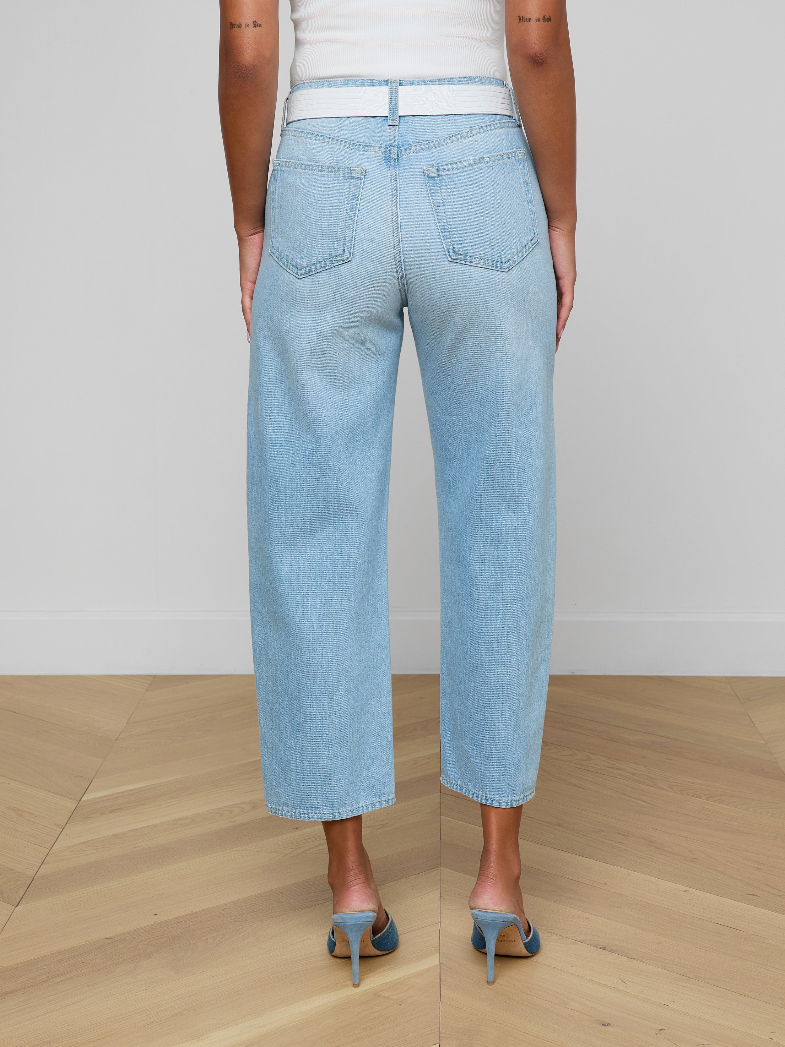 A person wearing the Mallis Bow-Leg Jean in a light wash and high heels stands with their back to the camera against a plain white background.