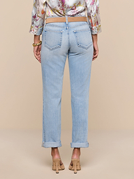 A person stands facing away against a plain white background, wearing the Ashby Low-Rise Slouch Jean in a vintage-inspired light wash, paired with a floral blouse and beige heels.