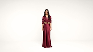 Woman stands in a long, deep red satin dress with a wide decorative belt and sunglasses against a plain white background.