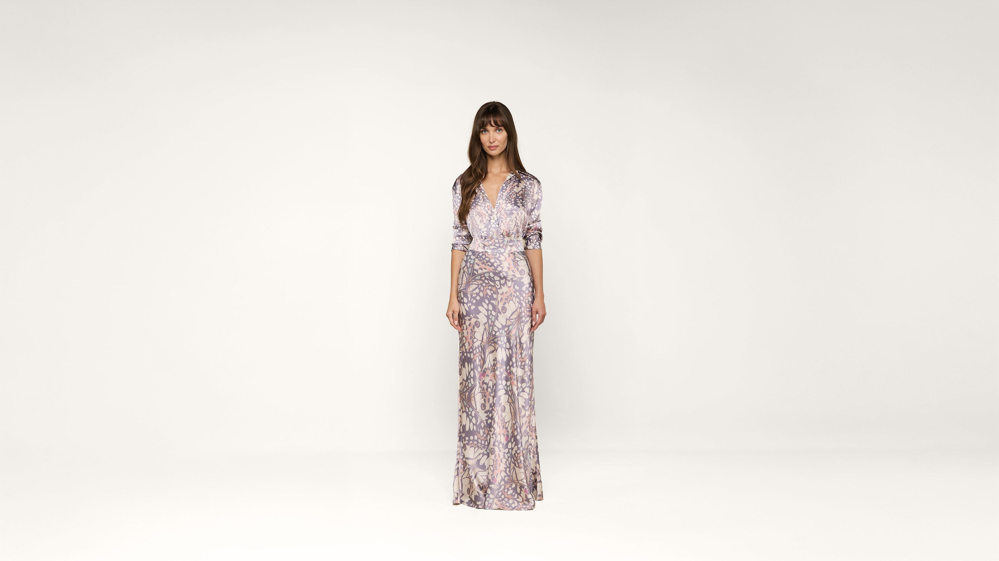 Woman standing in a long, patterned dress with sleeves rolled up, against a plain white background. She faces forward with a neutral expression.
