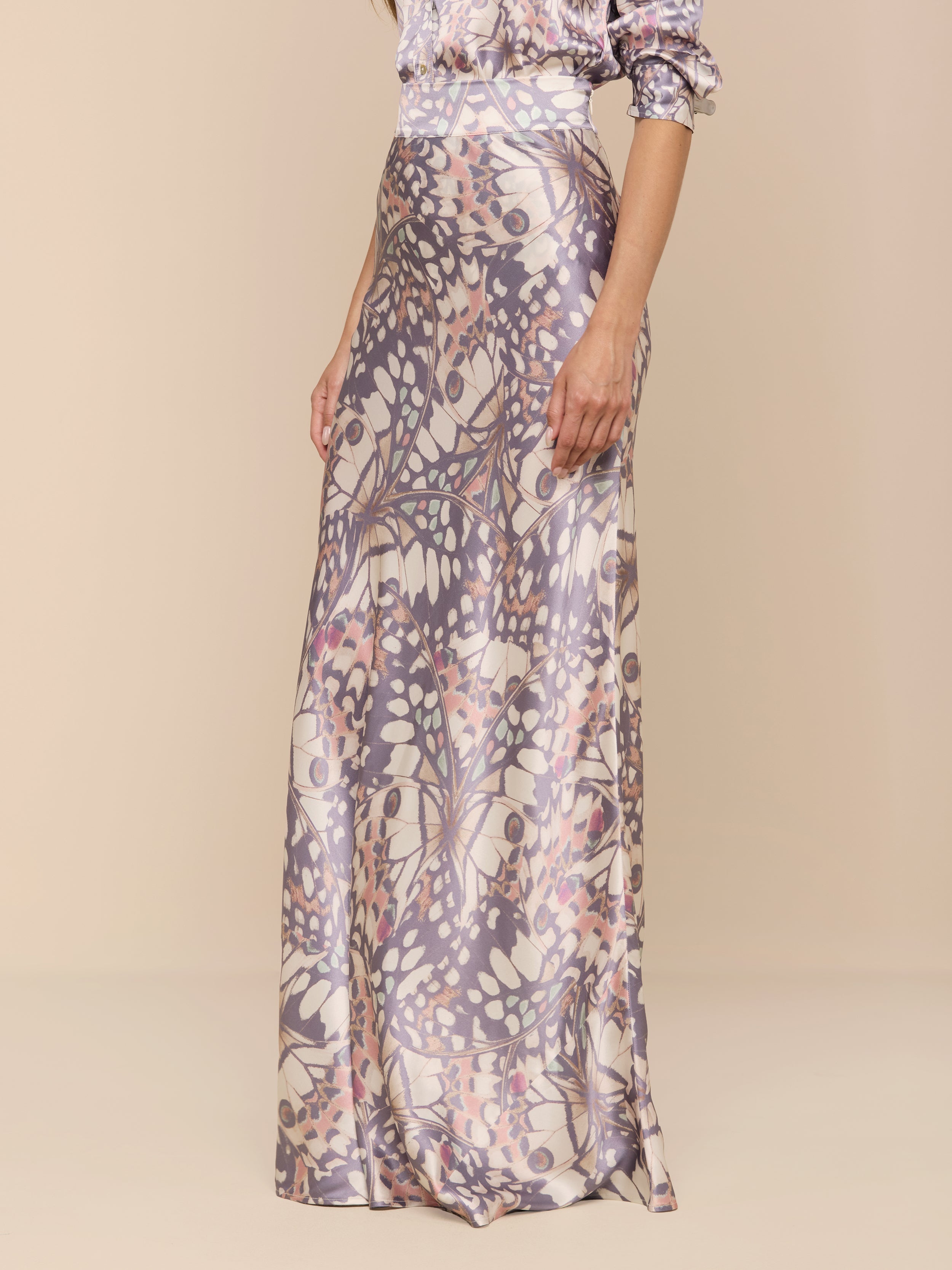 A woman models the Ryker Silk Maxi Skirt, featuring a pastel abstract floral pattern, while standing against a plain white background. Her head is not visible in the image.