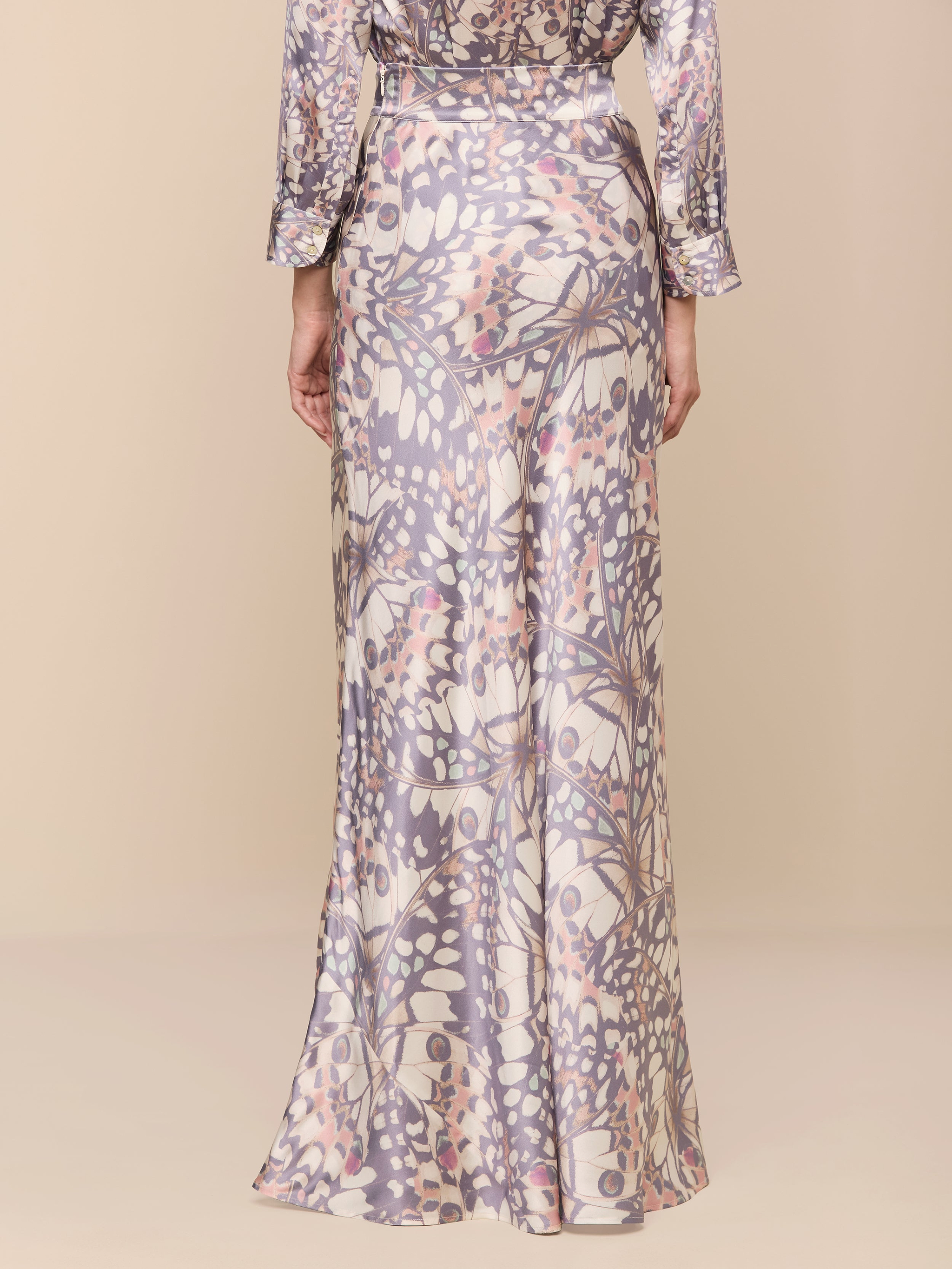 A person shown from the back is wearing the Ryker Silk Maxi Skirt—a long, flowy pure silk skirt featuring a pastel abstract floral pattern—while standing against a plain white background.