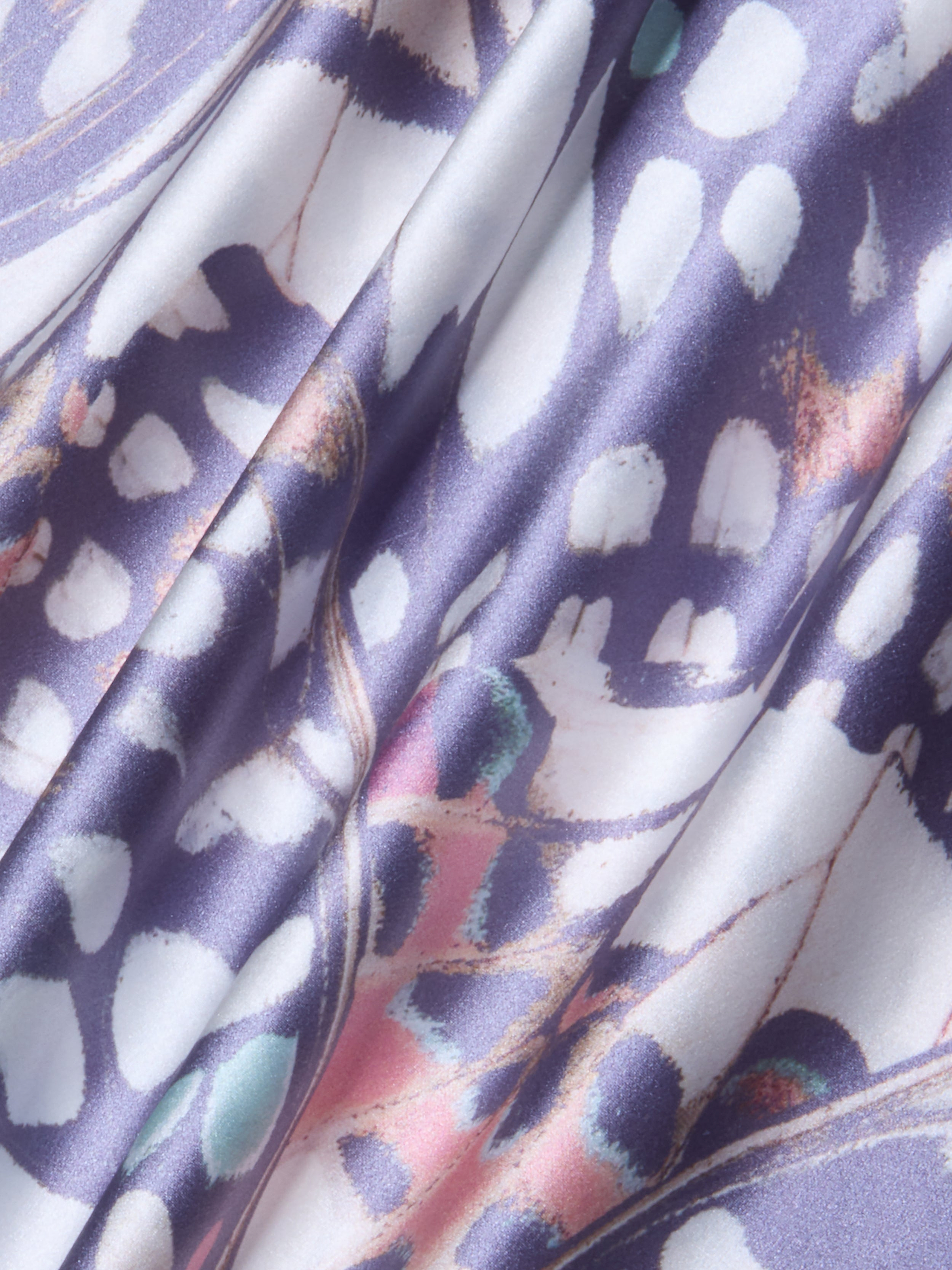 A close-up of the Ryker Silk Maxi Skirt, featuring draped silk charmeuse fabric with a colorful abstract pattern in purple, white, pink, and teal hues. The material looks smooth and shiny with soft folds and a mix of organic shapes and lines reminiscent of a butterfly wing print.