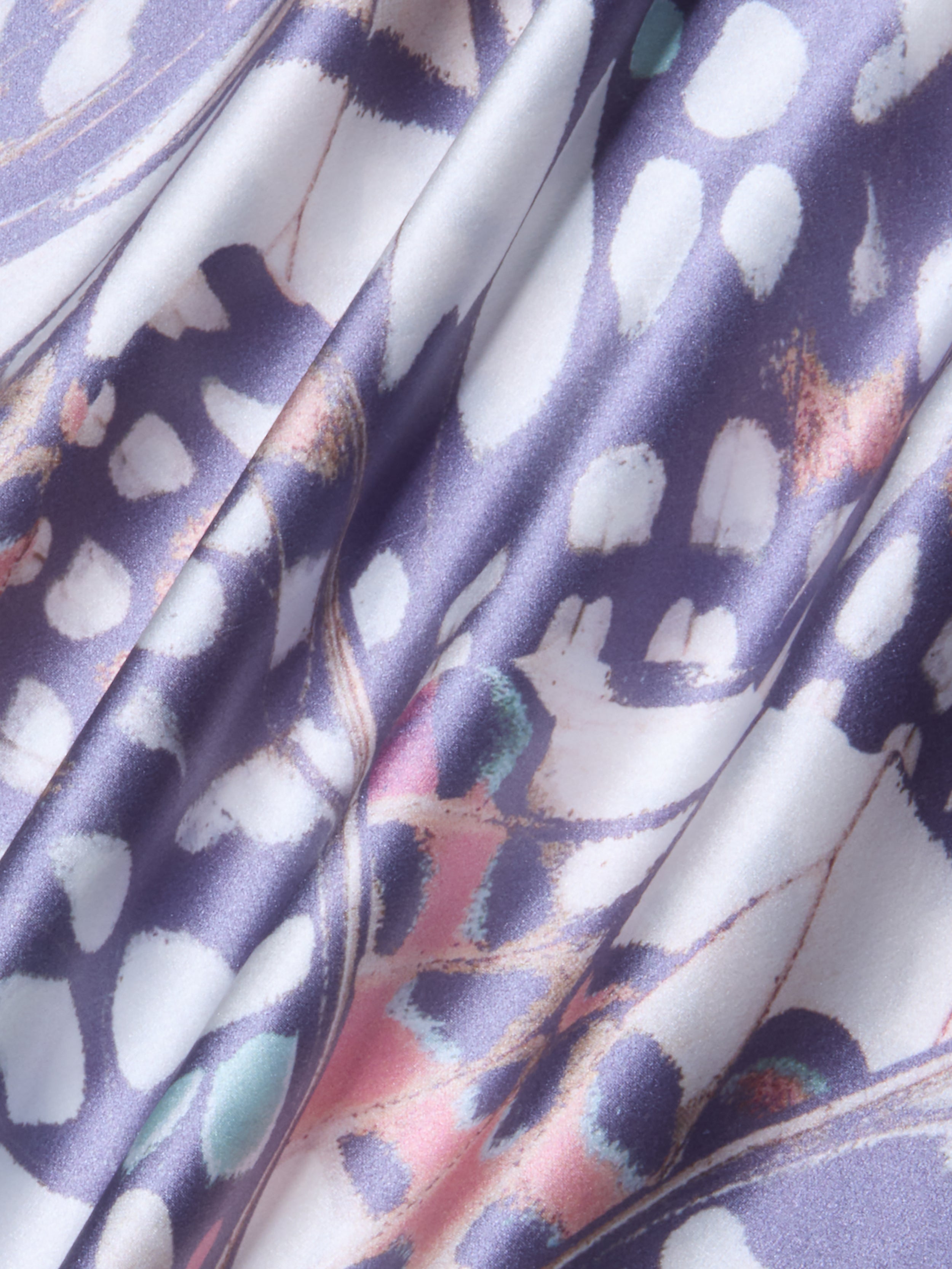 A close-up of the Ryker Silk Maxi Skirt, featuring draped silk charmeuse fabric with a colorful abstract pattern in purple, white, pink, and teal hues. The material looks smooth and shiny with soft folds and a mix of organic shapes and lines reminiscent of a butterfly wing print.