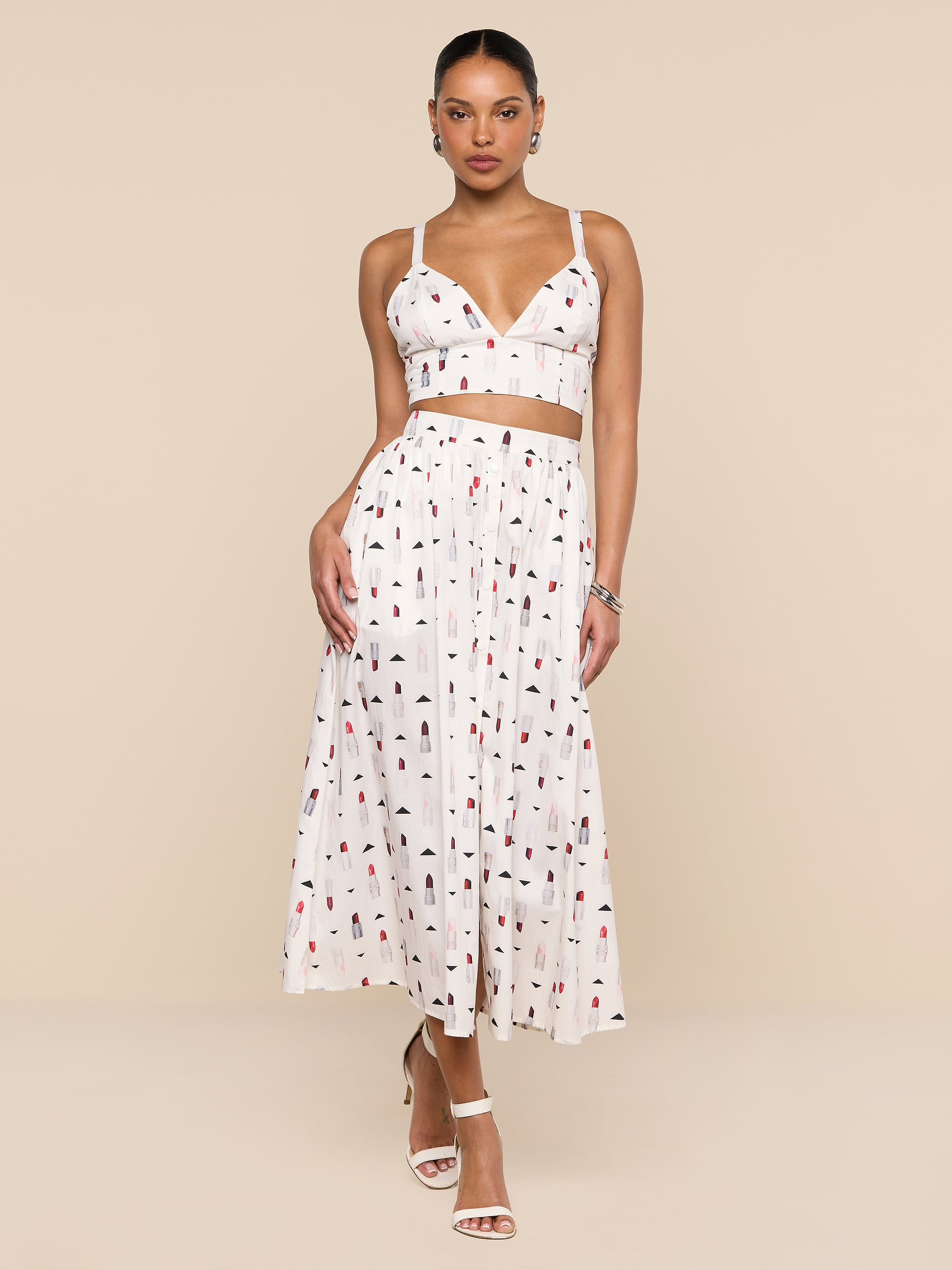 A woman wearing a white sleeveless crop top and the Seina Poplin Midi Skirt—a high-waisted, ankle-length skirt featuring a multicolored abstract print—stands against a plain white background.