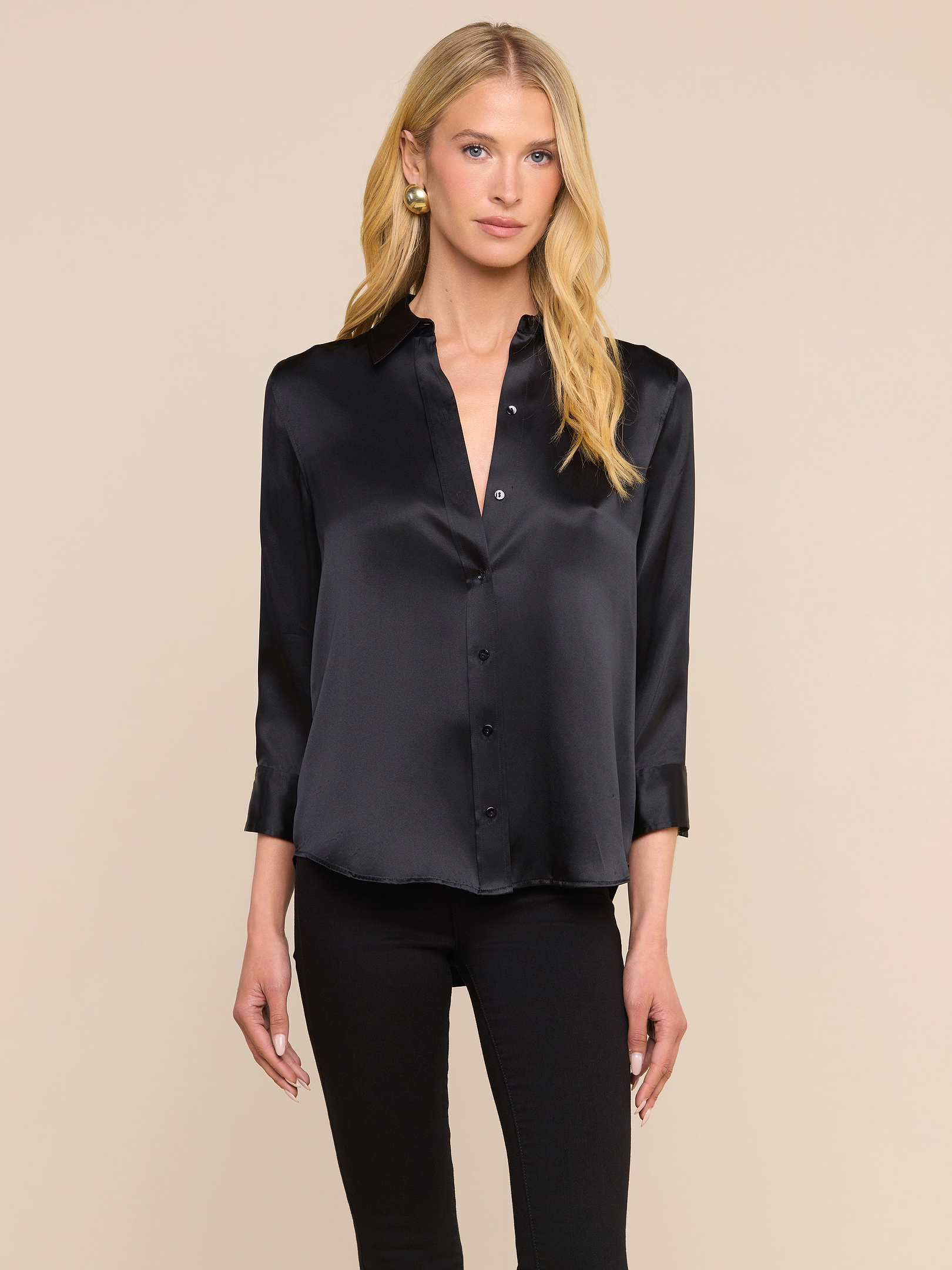 A woman stands facing forward against a plain light background, wearing the Dani Silk Blouse in black with three-quarter sleeves and black pants.