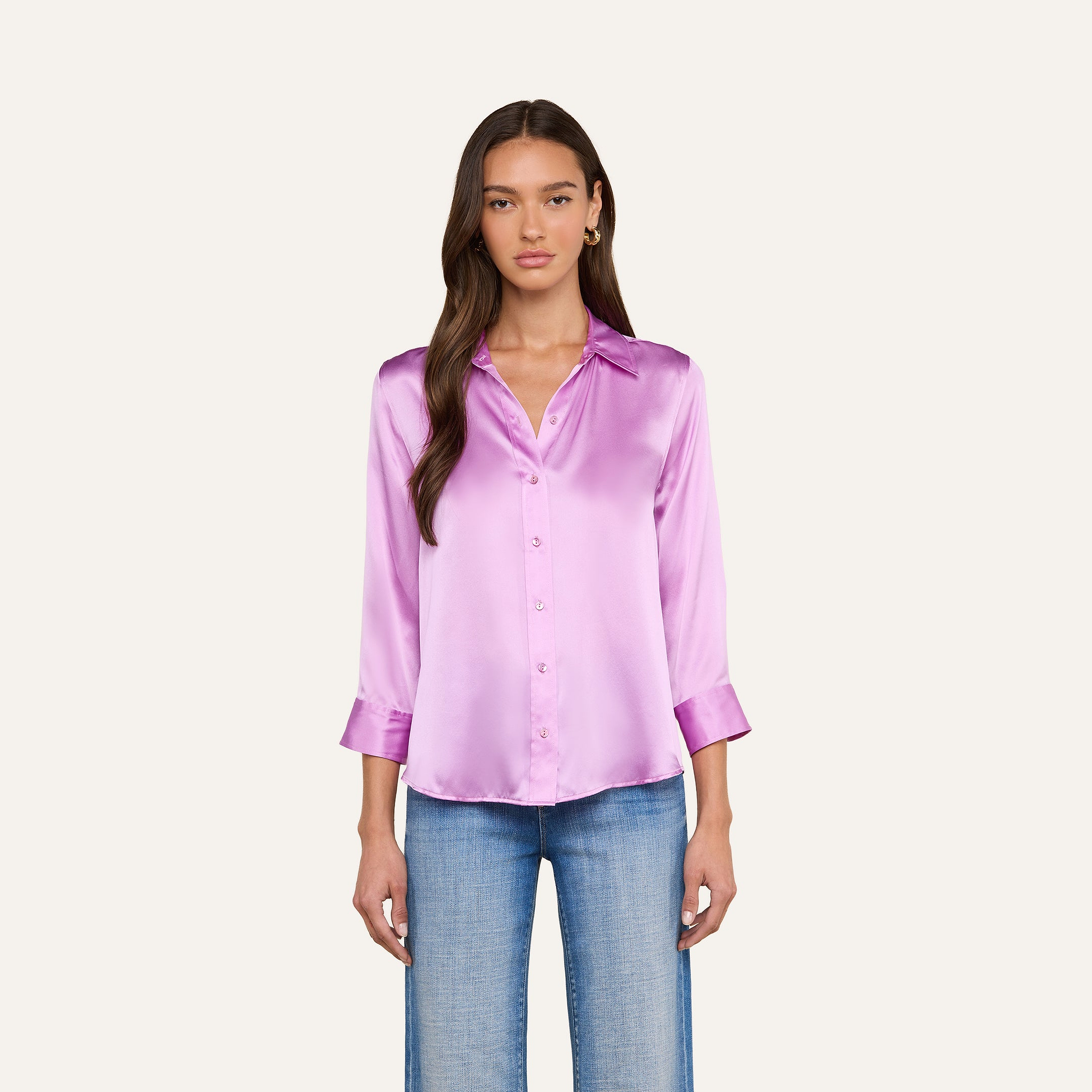 A woman stands facing forward against a plain background, wearing the shiny, light purple Dani Silk Blouse with three-quarter sleeves and blue jeans.
