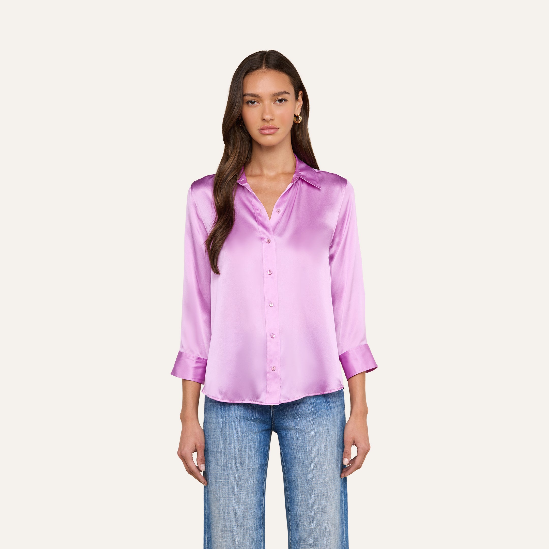 A woman stands facing forward against a plain background, wearing the shiny, light purple Dani Silk Blouse with three-quarter sleeves and blue jeans.