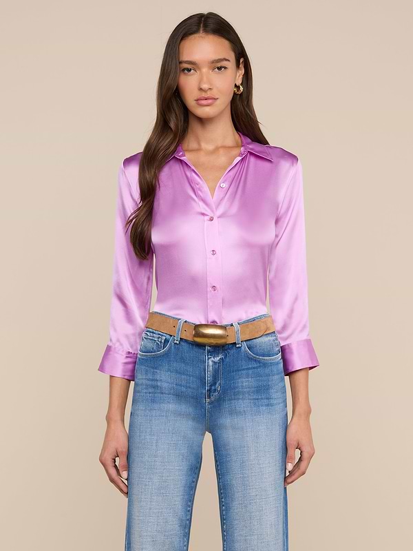 A woman with long brown hair wears the Dani Silk Blouse in a shiny, light purple silk charmeuse with three-quarter sleeves and pairs it with blue jeans, standing against a plain light background.