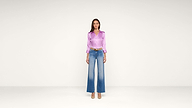 Woman standing against a plain white background wearing a shiny lavender blouse, wide-leg blue jeans with a faded effect, a brown belt, and beige heels.