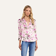 A woman wears the Dani Silk Blouse, a button-down top adorned with a pink rose print, paired with blue jeans and standing against a plain, light background.
