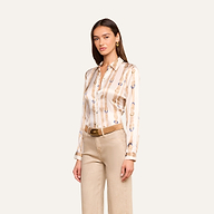 A woman wearing the Tyler Silk Blouse—a beige and gold patterned silk button-down with long sleeves—paired with tan wide-leg pants and a brown belt, standing against a plain light background.