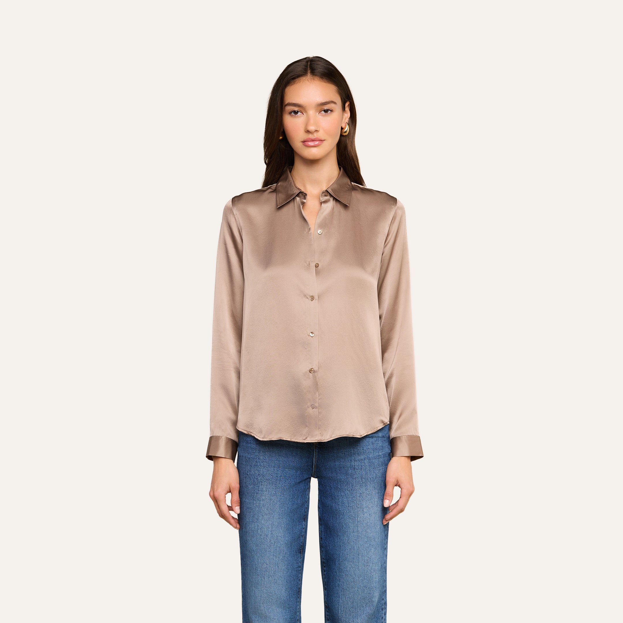 A woman stands facing forward wearing the Tyler Silk Blouse in cardamom brown, paired with blue jeans against a plain light background.