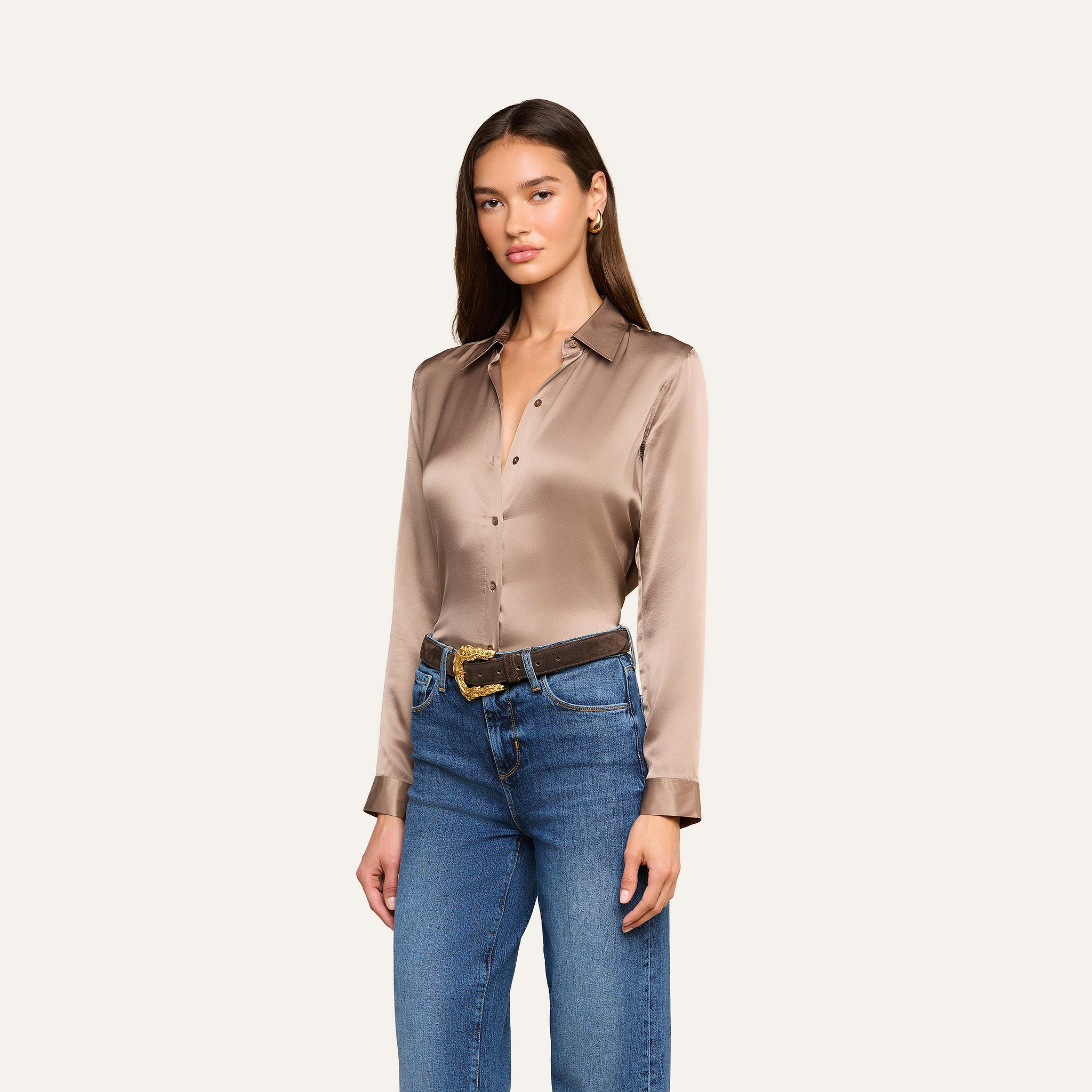 A woman wearing the Tyler Silk Blouse in cardamom brown, styled with blue jeans and a brown belt, stands against a plain light background.