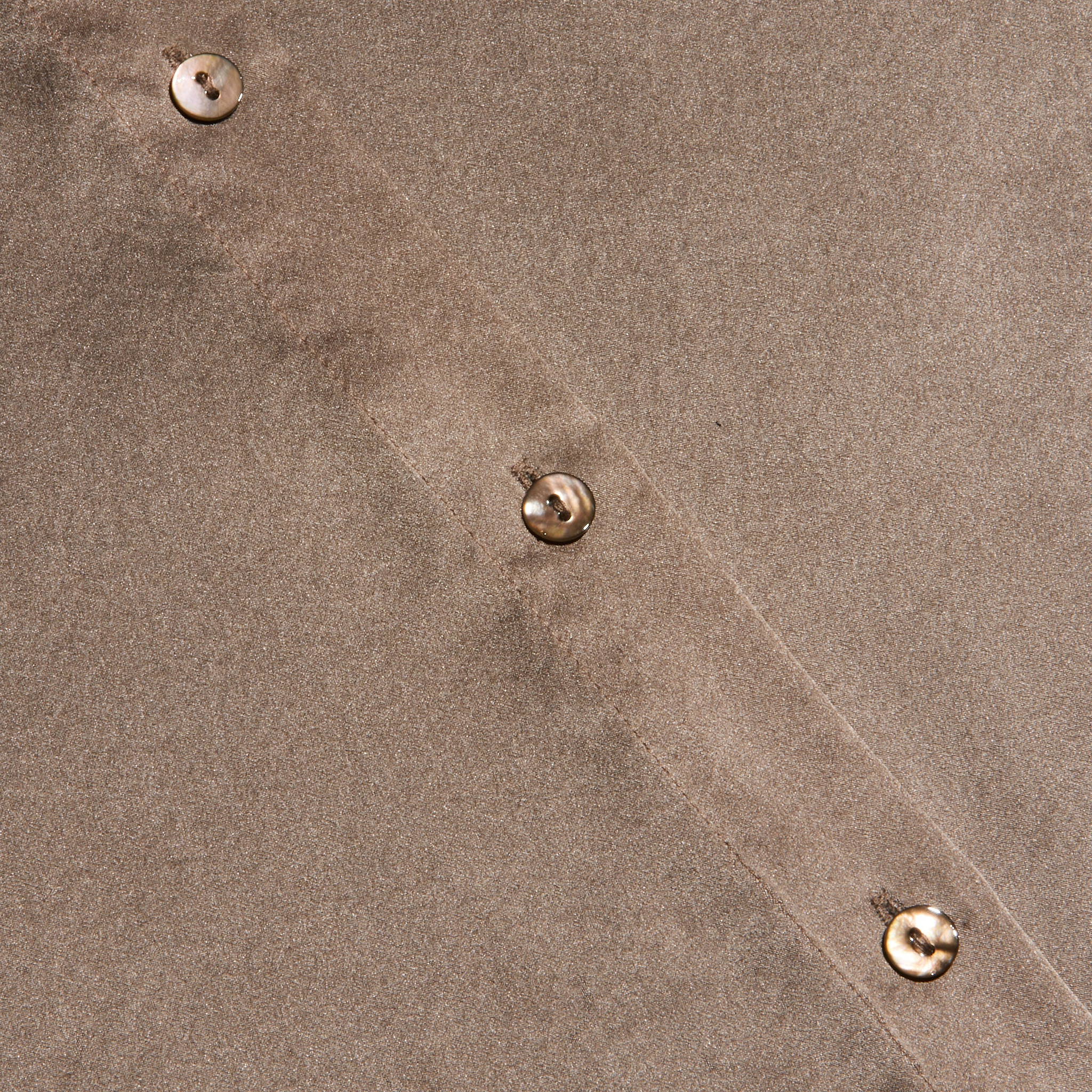Close-up of the Tyler Silk Blouse in cardamom brown, featuring four beige buttons sewn in a diagonal line. The texture of the silk fabric and precise stitching along the seam are clearly visible.