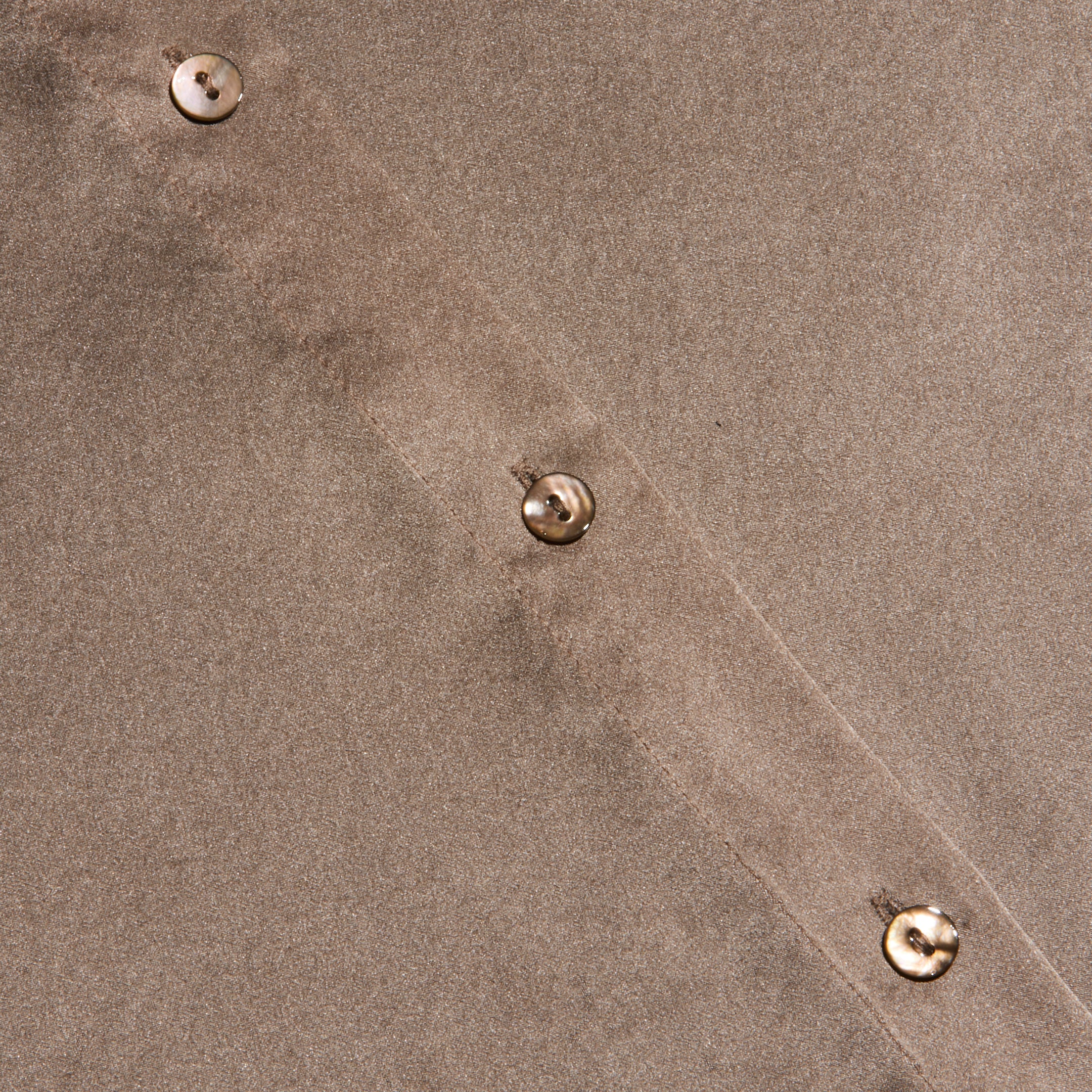 Close-up of the Tyler Silk Blouse in cardamom brown, featuring four beige buttons sewn in a diagonal line. The texture of the silk fabric and precise stitching along the seam are clearly visible.