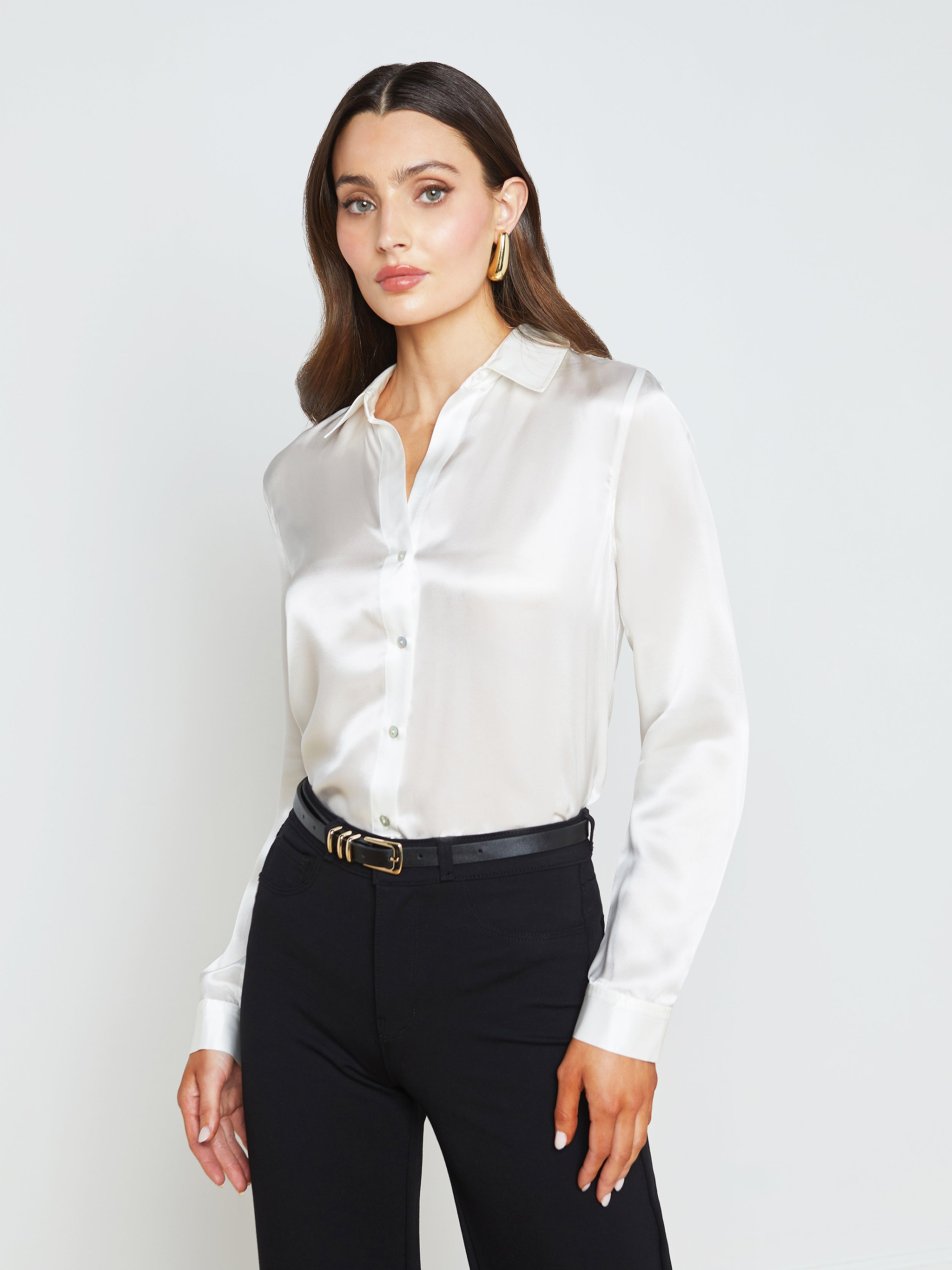 A woman wearing the Tyler Silk Blouse in ivory, paired with black pants and a black belt, poses against a plain light background.