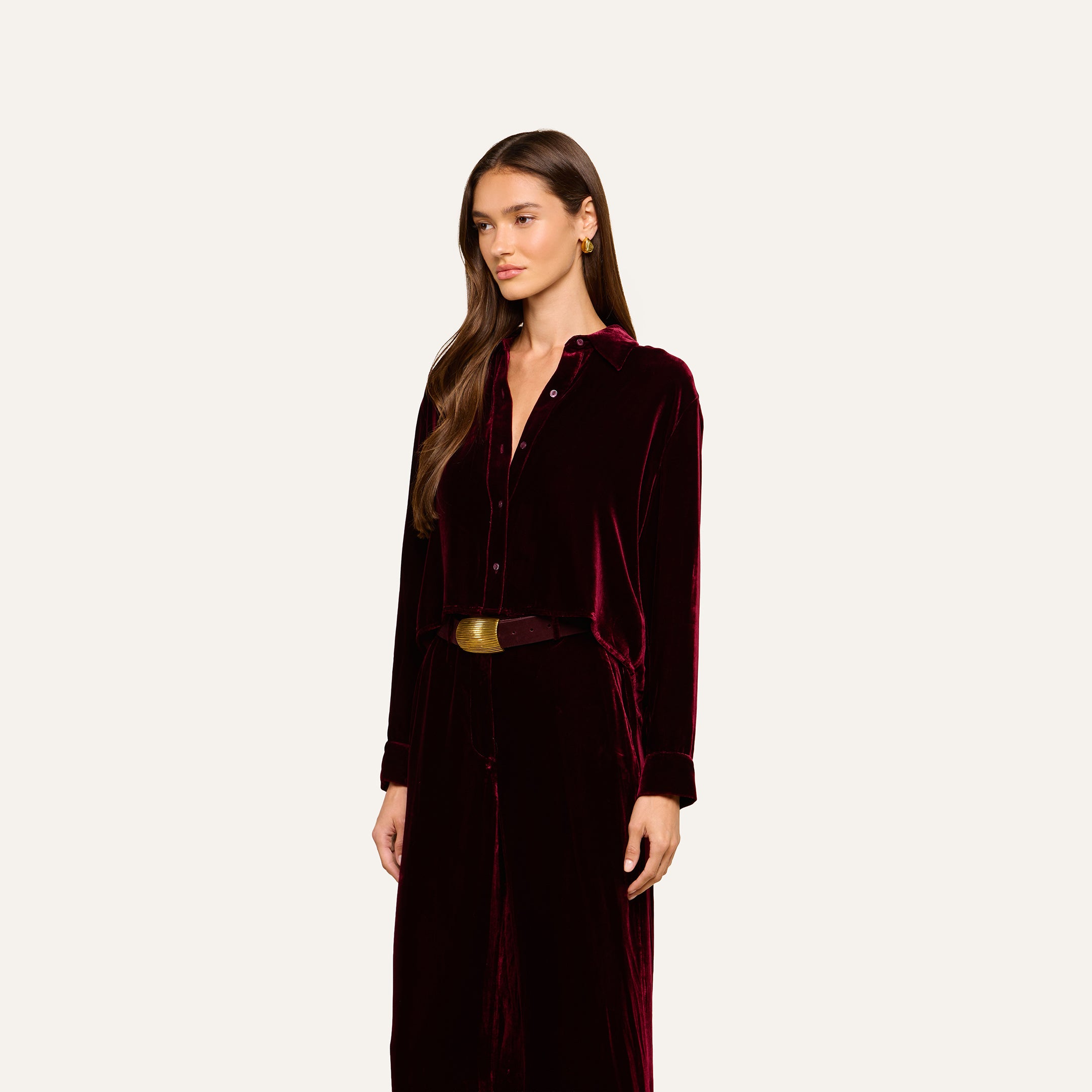 A woman wearing the Cosette Velvet Shirt, a long-sleeved dark red velvet dress with buttons and a wide belt, stands against a plain light background.