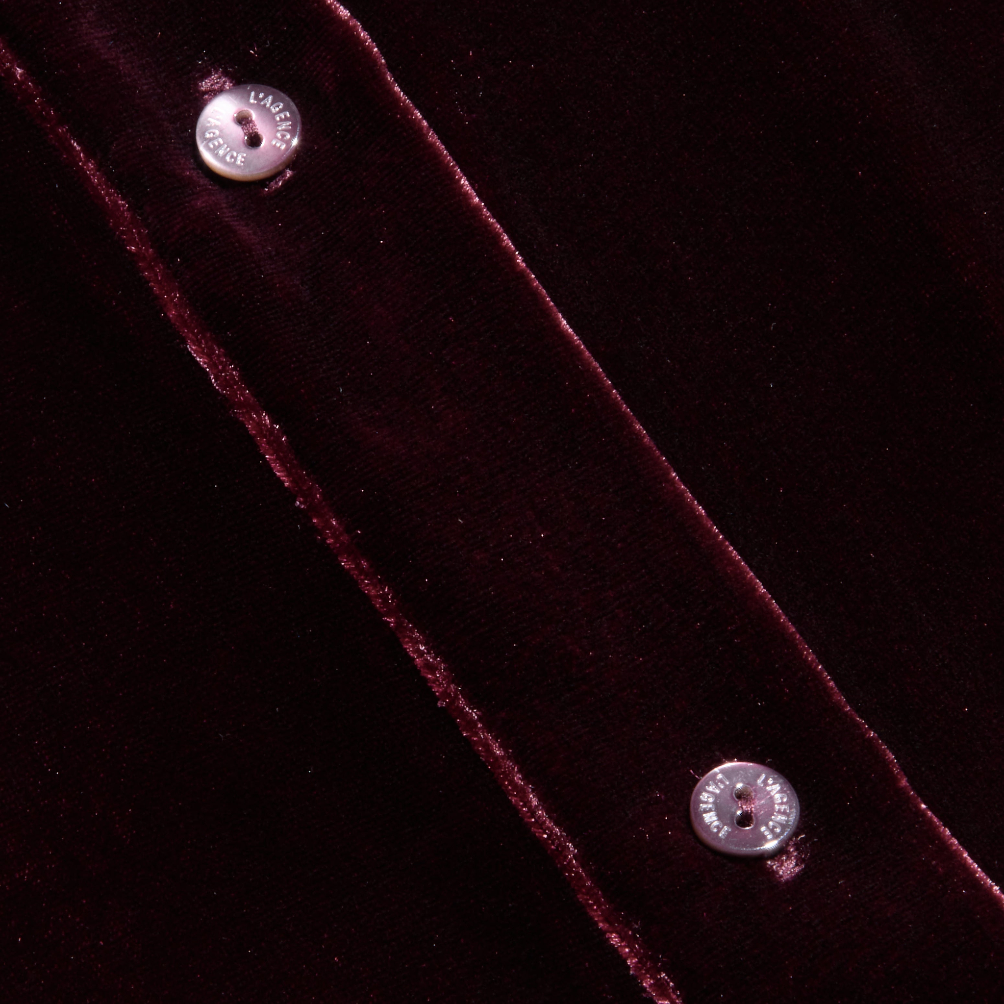 Close-up of the Cosette Velvet Shirt in dark red, featuring two silver snap buttons along a seam and highlighting the luxurious texture and sheen of the velvet fabric.