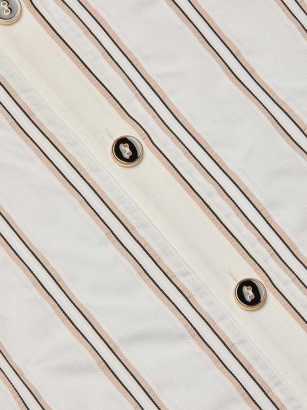 Close-up of the Cosette Shirt, crafted from white fabric with vertical beige and black jacquard stripes and accented by gold-rimmed black buttons sewn along the stripes, evoking a tailored look.
