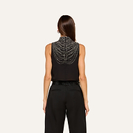 A person with straight brown hair wears the Yun Draped Crystal Tank—a sleeveless black blouse adorned with intricate beaded chains draping across the back—styled as an elegant evening top and paired with high-waisted black pants, shown from behind against a plain light background.
