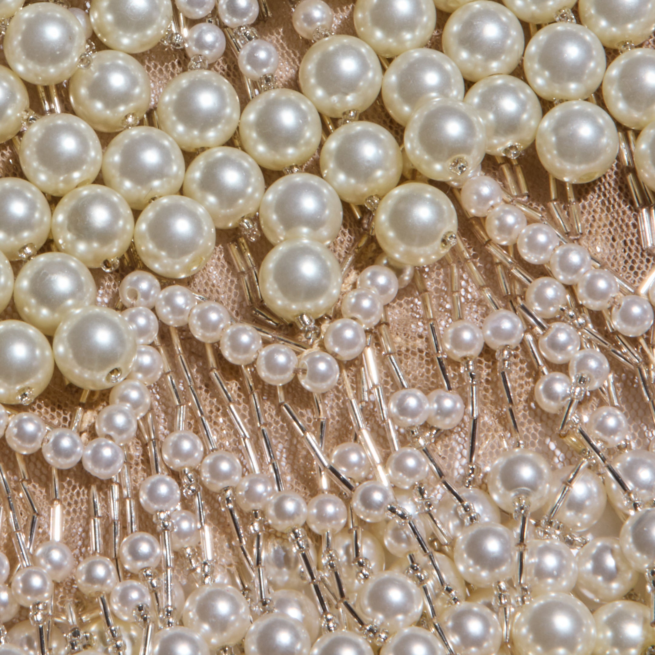 Close-up of rows of white pearls and small beads sewn onto a light, sheer mesh fabric with metallic threads, creating an intricate, decorative pattern reminiscent of the Rogan Pearl Fringe Top.