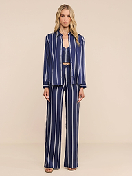 A person stands against a plain white background wearing the Livvy Trouser—a pair of high-rise, straight-leg navy blue trousers with vertical white stripes—paired with a matching button-up shirt and open-toe sandals.
