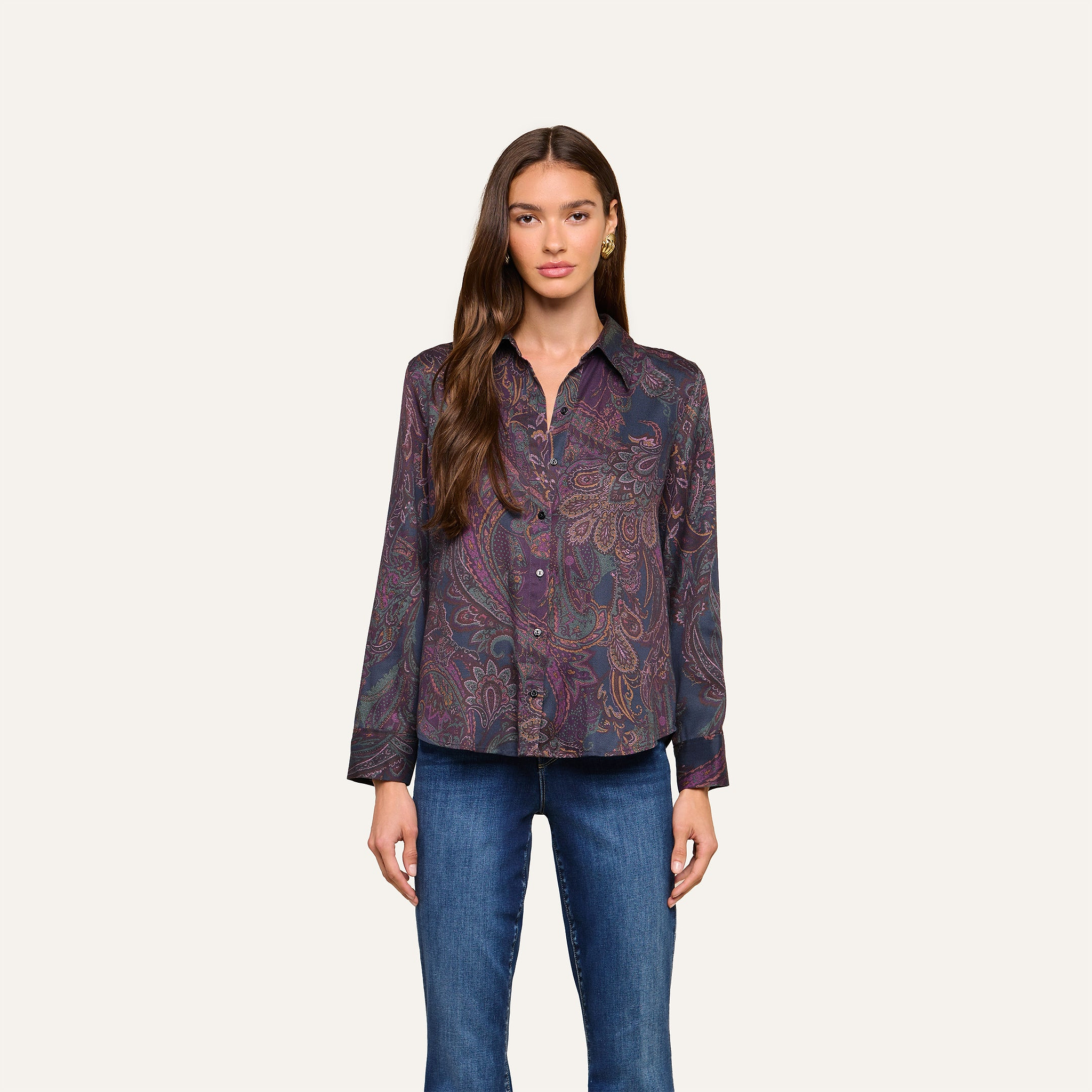 A woman stands facing forward, wearing the Ellery Button-Down Shirt in a dark paisley print and blue jeans, against a plain light background.