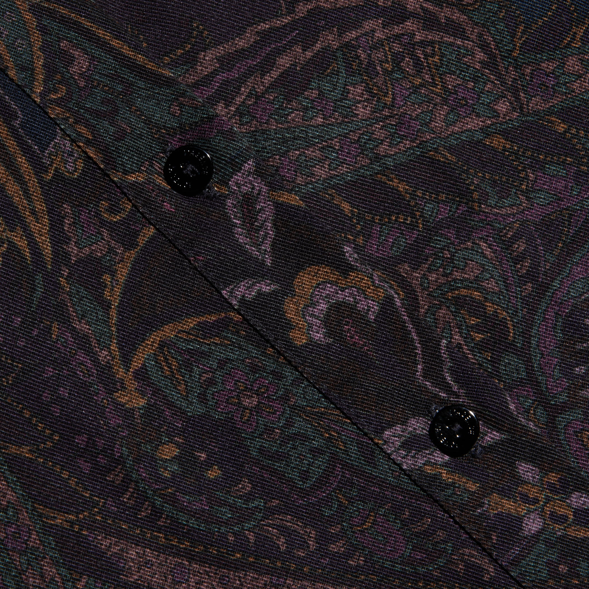 Close-up of the Ellery Button-Down Shirt made from a dark, patterned lightweight twill fabric featuring a muted paisley print and two black buttons sewn along a diagonal seam.