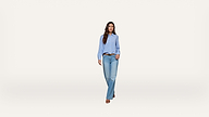 A woman wearing a blue striped shirt, light blue jeans, brown belt, and brown sandals walks toward the camera on a plain white background.
