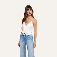 Woman wearing the Dara Stretch Satin Bodysuit with adjustable straps, paired with light blue jeans and a white belt with a large buckle, standing against a plain light background and looking slightly to her left.
